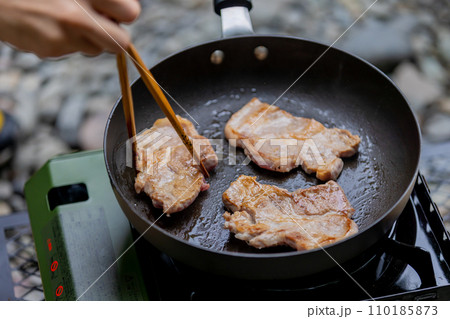 キャンプで豚肉を焼く男性　ガスコンロ 110185873