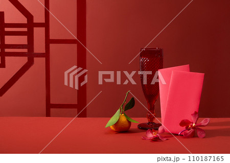 A glass decorated with a tangerine, small flowers and several red envelopes. Front view. Vacant space for product advertising A glass decorated with a tangerine, small flowers and several red envelopes. Front view. Vacant space for product advertising 110187165