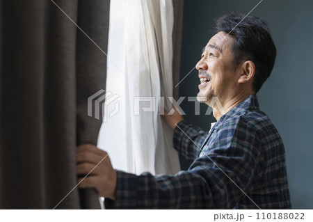 カーテンを開けるパジャマを着た50代の男性 110188022