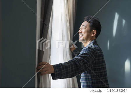 カーテンを開けるパジャマを着た50代の男性 110188044