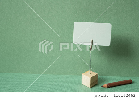 Memo pad with holder and colored pencil on desk. green wall background. copy space Memo pad with holder and colored pencil on desk. green wall background. copy space 110192462