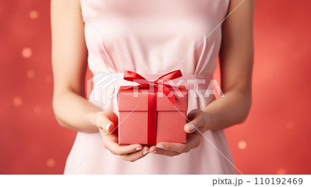 Women wearing pink dress holding a gift box in her hands on red background, giving present on New year and Valentines day. Generative AI 110192469