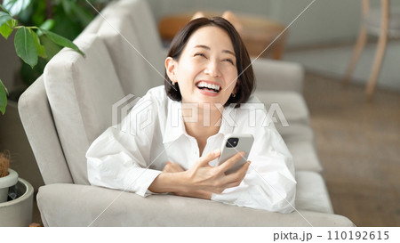 ソファーで横になってスマホを操作する女性 ソファーで横になってスマホを操作する女性 110192615