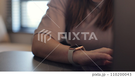Woman fingers does double tap on smart watch for hands-free interaction. Young woman is typing on laptop at the work table at the office. Woman fingers does double tap on smart watch for hands-free interaction. Young woman is typing on laptop at the work table at the office. 110200043