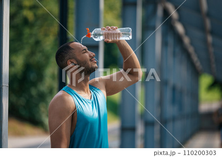Young dark-skinned athlete pouring some refreshing water on himself after workout Young dark-skinned athlete pouring some refreshing water on himself after workout 110200303