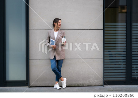 Woman with cocktail and notebook standing near modern building. Woman with cocktail and notebook standing near modern building. 110200860