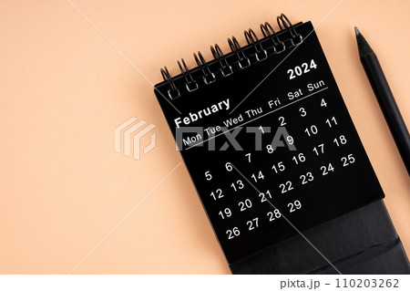 February 2024 Black spiral desktop calendar and wooden pencil. 110203262