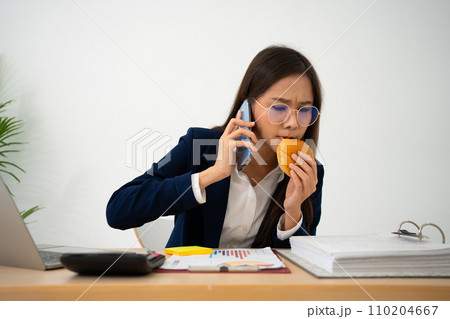 Busy and tired businesswoman eating Bread and milk for lunch at the Desk office and working to deliver financial statements to a boss. Overworked and unhealthy for ready meals, burnout concept. 110204667