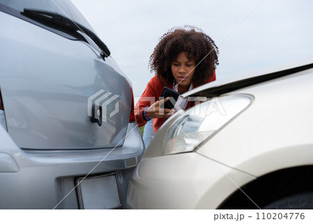 Half Thai African driver check for damage after a car accident before taking pictures and sending insurance. Online car accident insurance claim after submitting photos and evidence to an insurance. 110204776