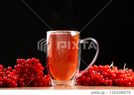 Hot viburnum tea in a glass cup with a double bottom on a black background. 110206678