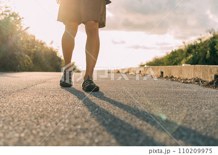 夕日に向かって歩く男性 110209975