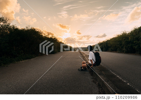 夕日に照らされた道に座る男性 110209986