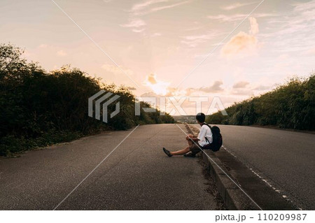 夕日に照らされた道に座る男性 夕日に照らされた道に座る男性 110209987