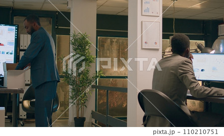 Upset worker holding box filled with desk belongings bidding farewell to colleague during last nightshift in office after being laid off. Sad businessman getting consoled after being fired from job 110210751