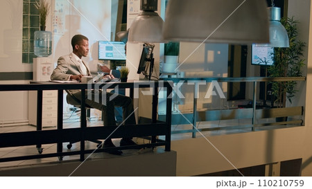 Management executive helping worker with auditing project task in office at night, laughing together. Business manager having fun with employee working with data charts during nightshift Management executive helping worker with auditing project task in office at night, laughing together. Business manager having fun with employee working with data charts during nightshift 110210759