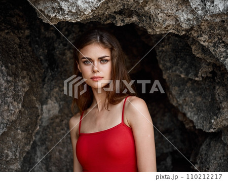Portrait of a woman in a red swimsuit against the rocks by the ocean, tanned skin from the sun, the concept of protecting skin from the sun and body health 110212217