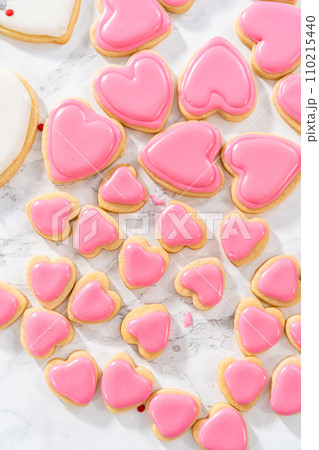 Decorating heart-shaped sugar cookies with pink and white royal icing for Valentine's Day. 110215440