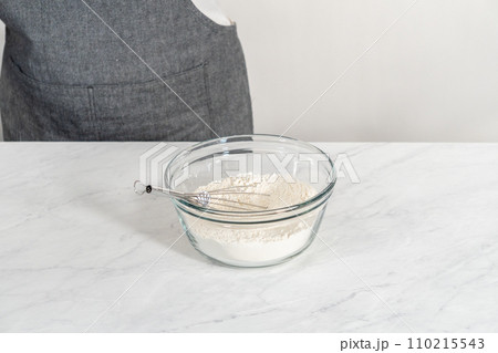 Mixing dry ingredients with a hand whisk in a glass mixing bowl to bake white chocolate macadamia nut. Mixing dry ingredients with a hand whisk in a glass mixing bowl to bake white chocolate macadamia nut. 110215543