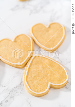 Decorating heart-shaped sugar cookies with pink and white royal icing for Valentine's Day. 110215544