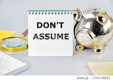DO NOT ASSUME A word, a text written on a notebook next to a piggy bank, a magnifying glass, a calculator, stickers 110218683