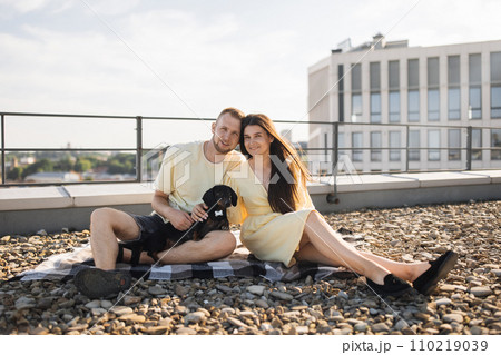 Excited couple sitting in embrace and caressing dog on roof Excited couple sitting in embrace and caressing dog on roof 110219039