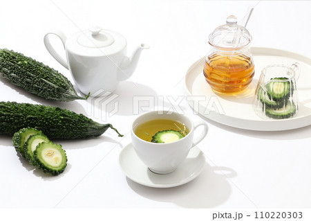 A tea set, fresh bitter melon and glassware are displayed on a white background. Bitter melon tea can help detoxify the liver and cleanse the intestines. 110220303