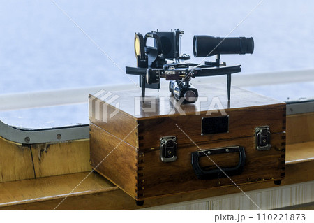 Nautical black sextant placed on wooden box in navigational bridge. Navigational equipment. Celestial navigation. 110221873