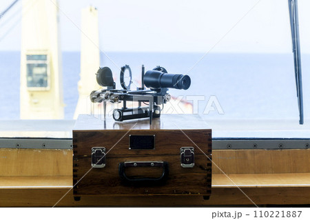 Nautical black sextant placed on wooden box in navigational bridge. Navigational equipment. Celestial navigation. 110221887