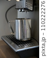 Coffee machine flushes hot water into a silver milk jug 110222276