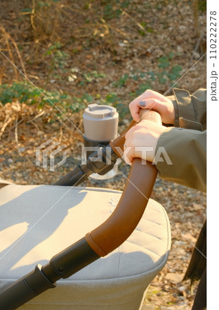 Hands pushing stroller with coffee mug, Germany 110222278