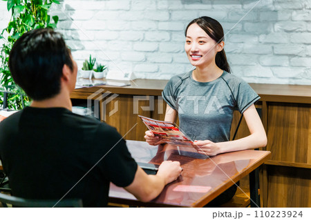 スポーツジムで入会案内を受ける女性 110223924