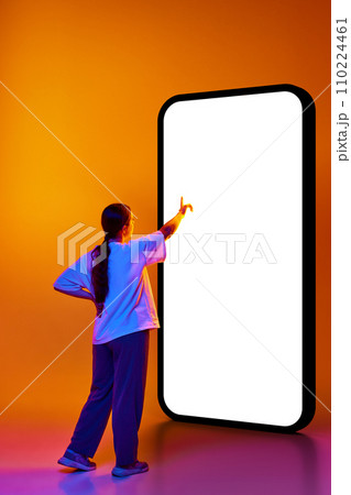 Back view photo of smart girl, student dressed in casual outfit pointing to huge smartphone with blank screen isolated gradient background. Back view photo of smart girl, student dressed in casual outfit pointing to huge smartphone with blank screen isolated gradient background. 110224461