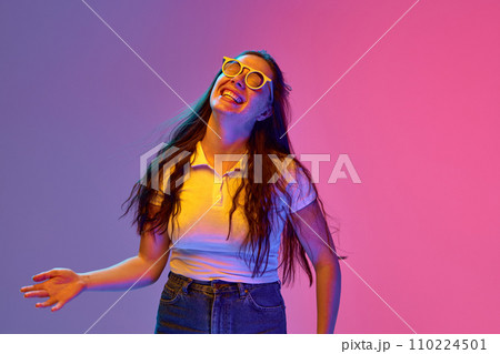 Portrait of positive, charming young brunette woman in sunglasses smiling an laughing against gradient background in neon light. Concept of emotions. 110224501
