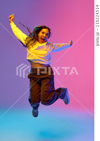Full-length portrait of young positive woman jumping of joy against gradient purple-blue-pink background. Concept of human emotions. Full-length portrait of young positive woman jumping of joy against gradient purple-blue-pink background. Concept of human emotions. 110224514