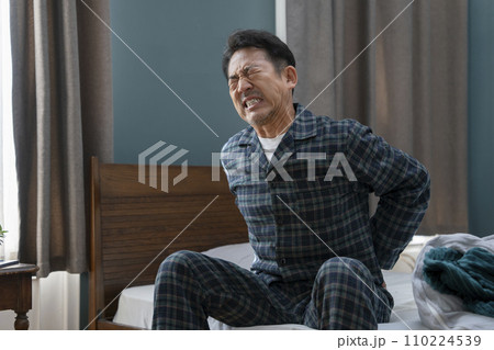 ベッドに座って腰に手をあてる50代の男性 腰痛 ギックリ腰 イメージ ベッドに座って腰に手をあてる50代の男性 腰痛 ギックリ腰 イメージ 110224539