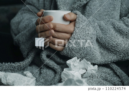 ill man warms up with a cup of hot herbal tea 110224574