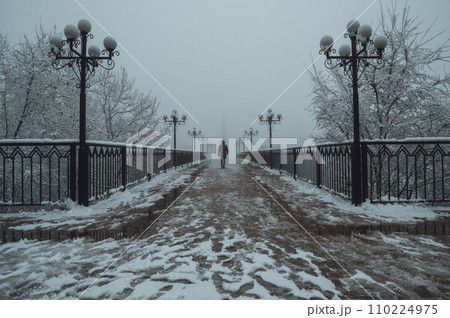 silhouette back man maniac walks on foggy bridge with lanterns in winter with snow and fog silhouette back man maniac walks on foggy bridge with lanterns in winter with snow and fog 110224975