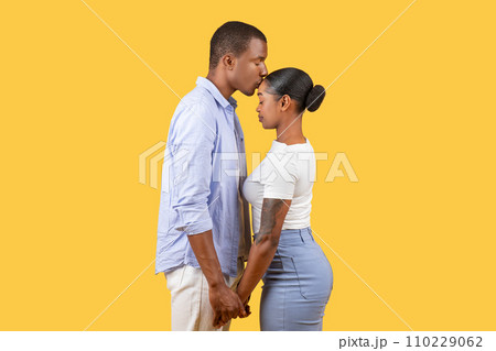 Intimate black couple holding hands, foreheads touching, yellow backdrop 110229062