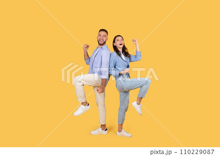 Emotional young couple shaking clenched fists, looking at camera with excitement, celebrating win on yellow background 110229087