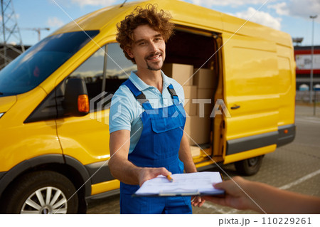 Portrait of friendly smiling young courier giving clipboard with pen for signature 110229261