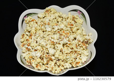 Delicious popcorn lies in a plate on a dark background. Delicious popcorn lies in a plate on a dark background. 110230579