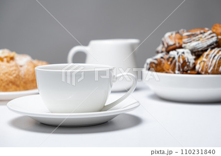 Breakfast utensils. An empty coffee cup, a milk jug and plates of croissants and scones Breakfast utensils. An empty coffee cup, a milk jug and plates of croissants and scones 110231840