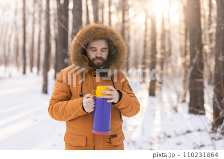 Close-up portrait handsome bearded millennial man in winter clothes and with thermos snow outdoor. Cold season and hot beverage in winter time, Copy space 110231864