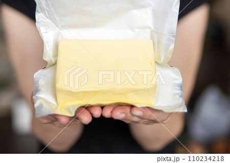 A hand holds butter in a pack close-up. Process of making sandwiches with butter. A hand holds butter in a pack close-up. Process of making sandwiches with butter. 110234218