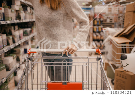 Beautiful woman with basket in supermarket. Portrait of a young girl in a market store with a shopping cart. Customer pushing a shopping cart at the grocery store, hands close up. Beautiful woman with basket in supermarket. Portrait of a young girl in a market store with a shopping cart. Customer pushing a shopping cart at the grocery store, hands close up. 110234321