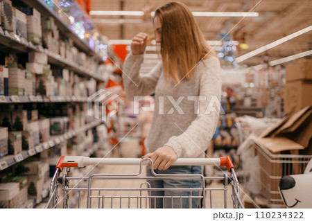 Beautiful woman with basket in supermarket. Portrait of a young girl in a market store with a shopping cart. Customer pushing a shopping cart at the grocery store, hands close up. Beautiful woman with basket in supermarket. Portrait of a young girl in a market store with a shopping cart. Customer pushing a shopping cart at the grocery store, hands close up. 110234322