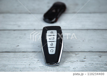 The car keys are black with metal inserts and automatic buttons on the background of white wood, on top of the keys is a black car in focus. High quality photo The car keys are black with metal inserts and automatic buttons on the background of white wood, on top of the keys is a black car in focus. High quality photo 110234400
