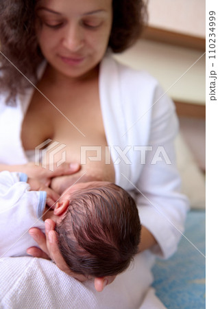 Beautiful happy loving young mother smiles while connects with her newborn baby, holds him in her arms, breastfeeds him 110234999