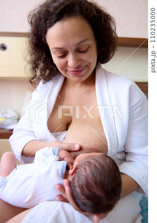 Young curly haired multi ethnic woman mother holding and breastfeeding her newborn baby. Maternity lifestyle 110235000