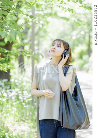 新緑の中ヘッドフォンで音楽を聴く若い女性 110235852